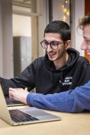 Een man legt iets uit aan een andere man aan een bureau met laptop