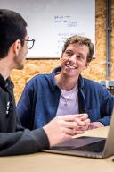 Jongen en man praten met elkaar aan een bureau met laptop voor zich